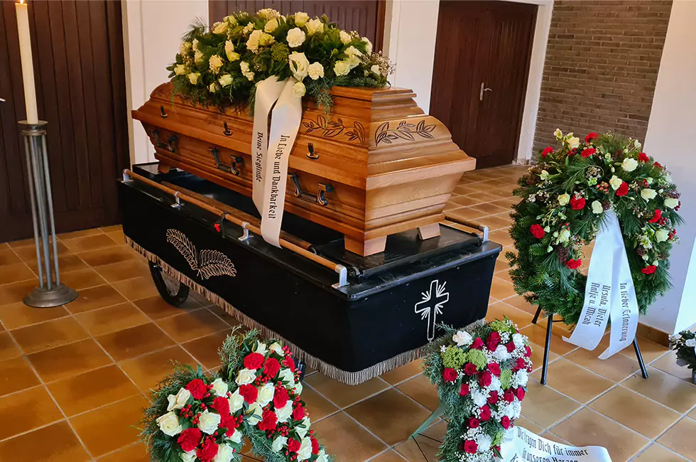 Weiße Rosen auf Holzsarg bei Bestattungsfeier