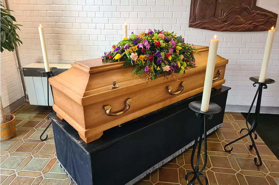 Bunte Blumen auf Holzsarg bei Bestattungsfeier