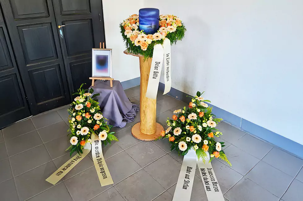 Blaue Urne und bunte Blumen bei Trauerfeier