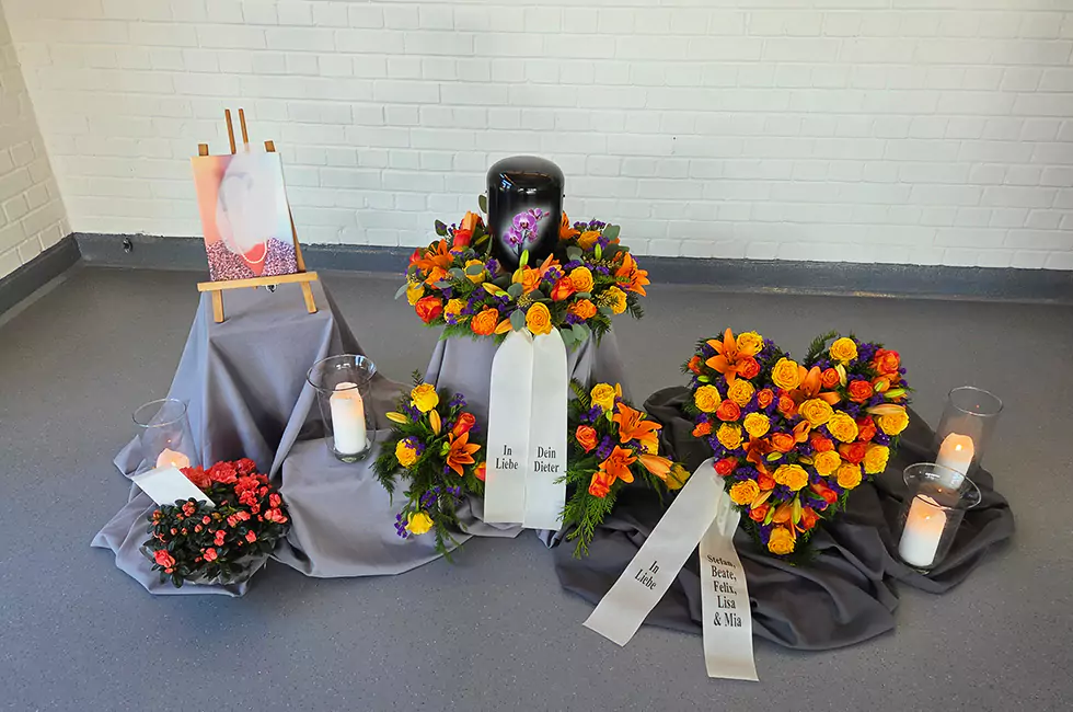 Schwarze Urne und bunte Blumen bei Trauerfeier